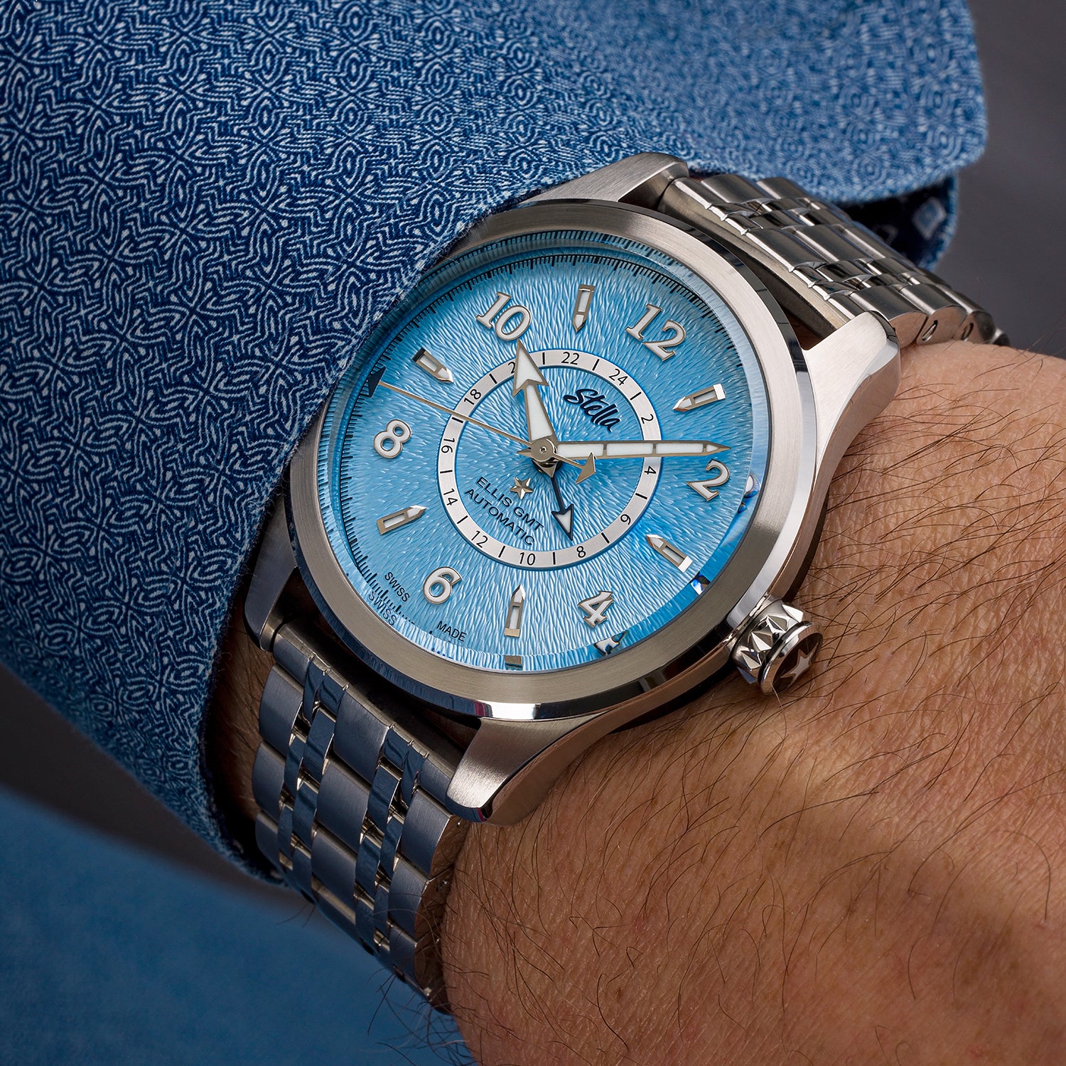 Wristwatch with blue face and silver case on a wrist, against a blue textured background